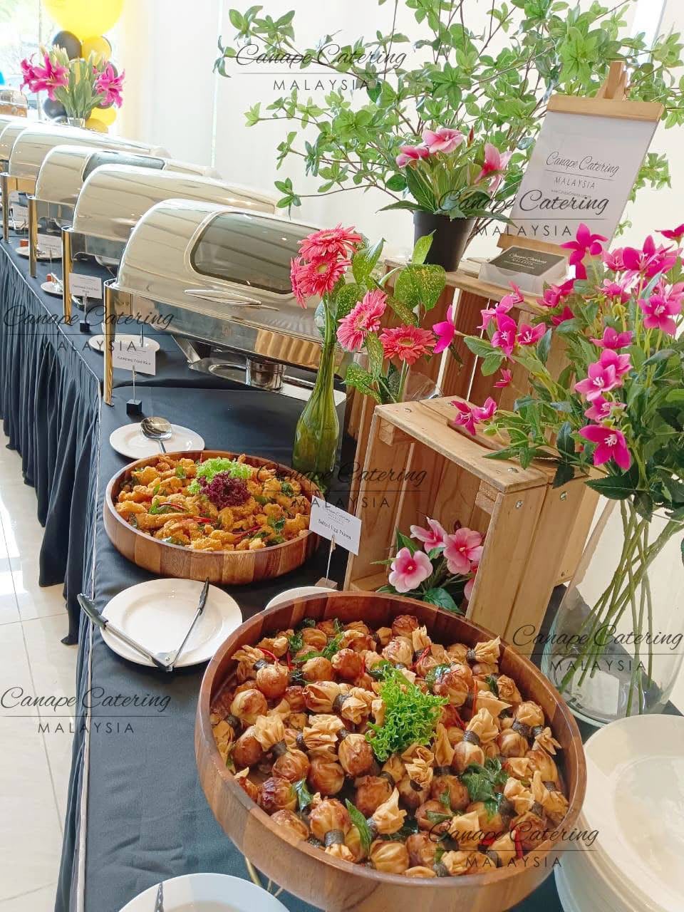 Buffet line with chafing dishes, wooden serving bowls and fresh flowers