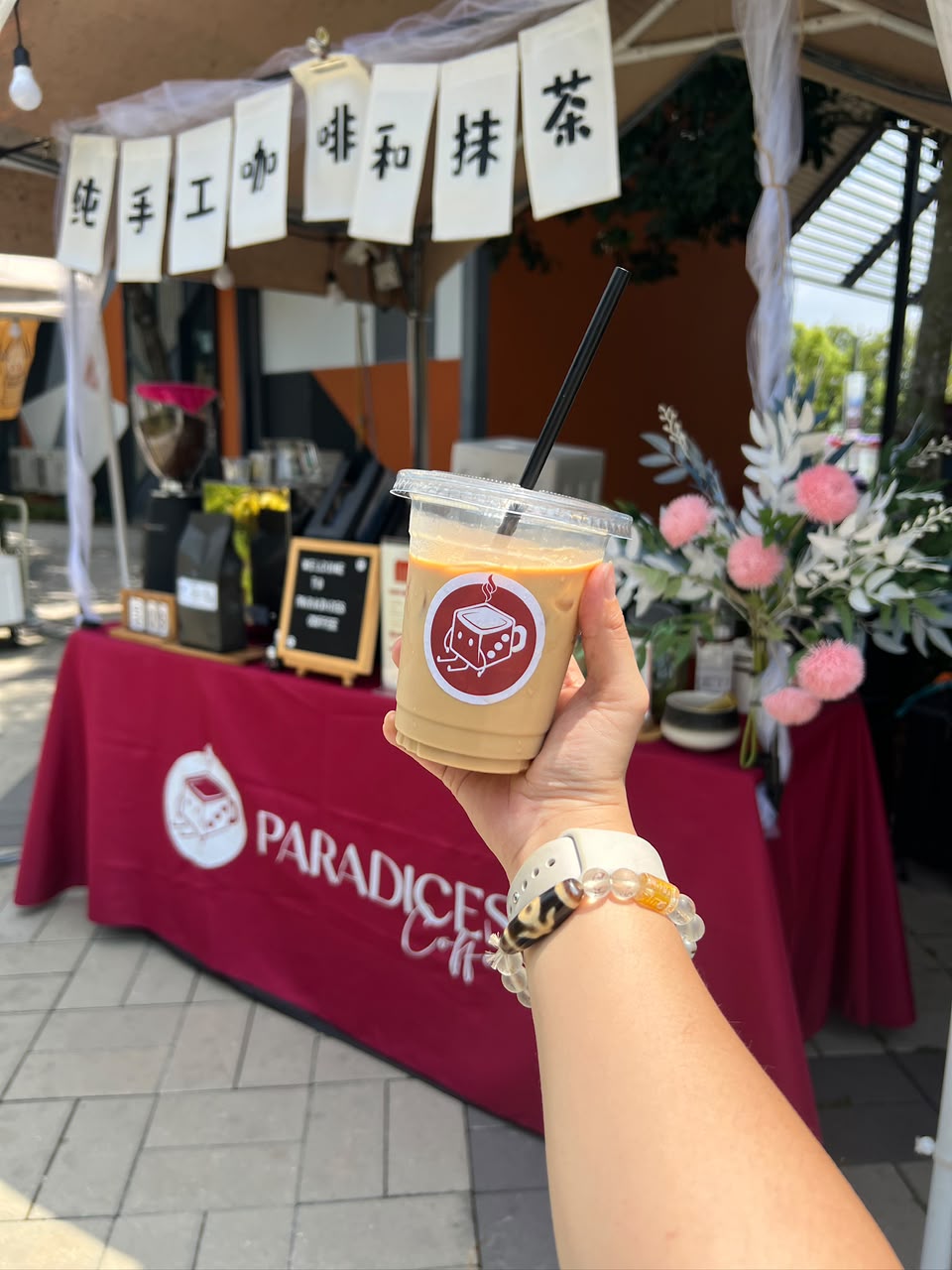 Iced latte with the Paradices logo held in front of the coffee booth